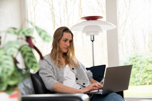 Kvinde sidder i sofa med sin bærbar computer på skødet