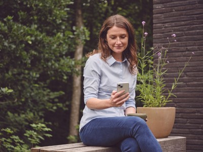 Kvinde i haven med mobiltelefon i hånden.
